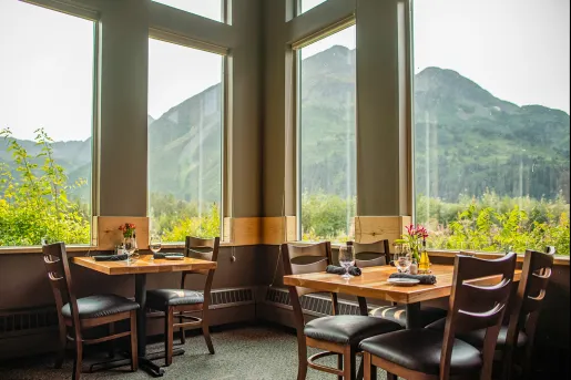 Dining room with two square tables and tables next to windows, looking out to large mountains