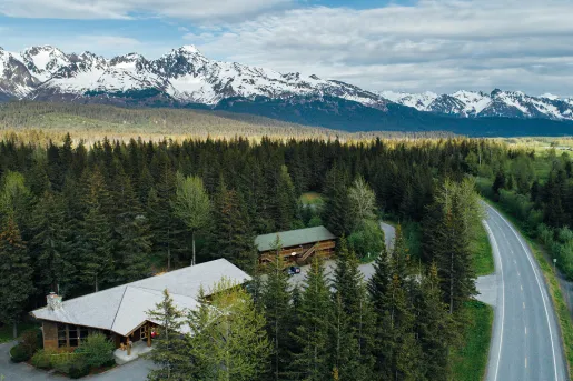 Large forest with a hotel building an a road to the right, with snow-capped mountains in the background