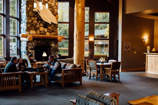 Cabin lobby with large wooden pillars and people sitting in front of a stone fireplace