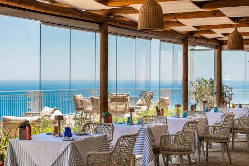 Indoor dining area with large, glass walls looking out to a balcony by the beach