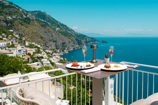 Outdoor balcony with a table full of food, looking out towards the ocean and hills