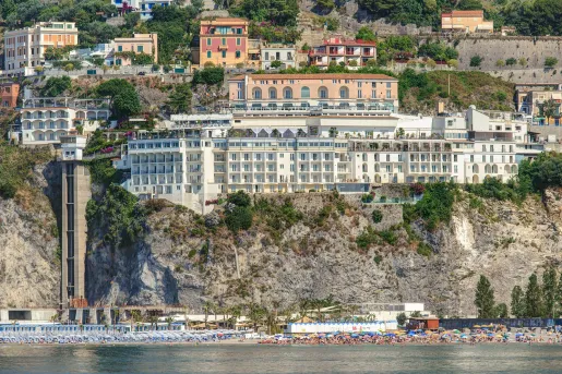 Exterior view of large hotel complex on a cliff, with the beach on the ground level
