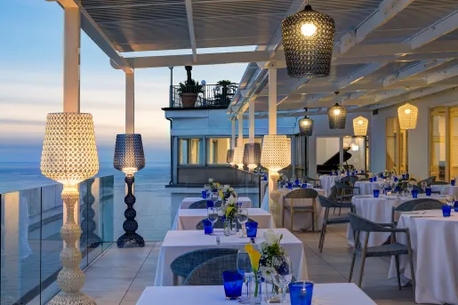 Outdoor patio and dining area, with wine glasses on each table and light fixtures surrounding the tables