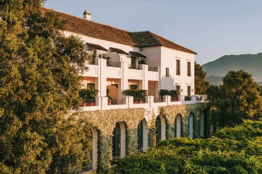 Exterior view of white and brown building, covered in plants and surrounded by trees