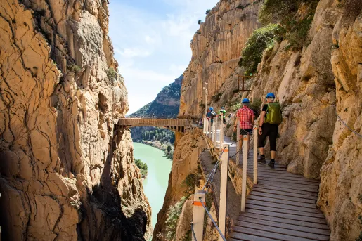 Group of people walking on a wooden bridge in between two large cliffs