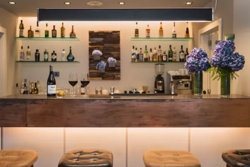 Bar counter with alcohol on the shelves along the wall and cushioned stools in front