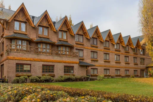 Exterior view of brick hotel building with a grass field and yellow trees in front