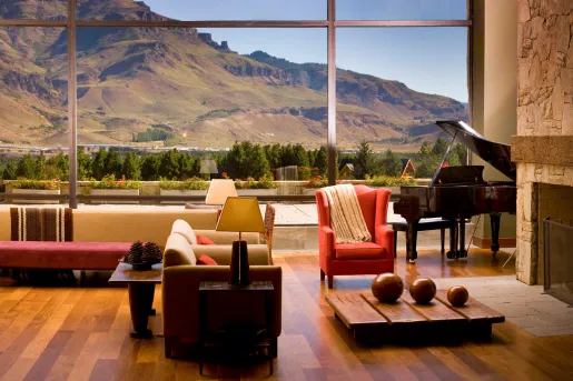 Indoor lobby with cushioned chairs, with large windows looking out to tall hills
