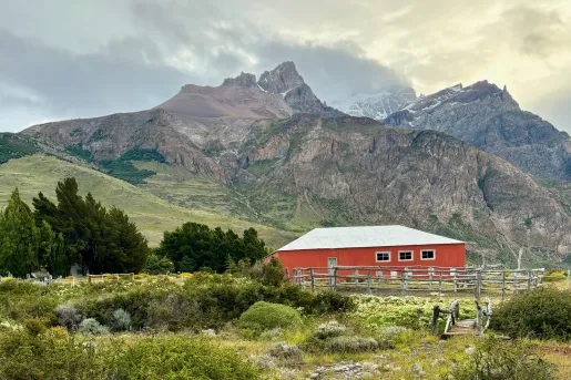 Red barn building in the middle of a grassy valley, with large mountains in the background