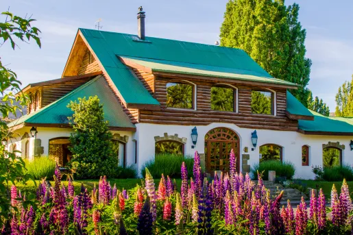 Cabin-style house with a green roof and pink flowers in front