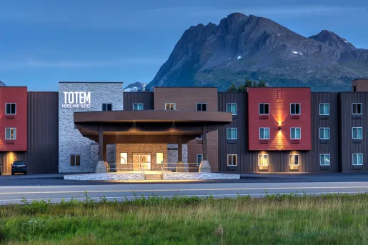 Exterior view of red, black and brown hotel buildings with large mountains in the background