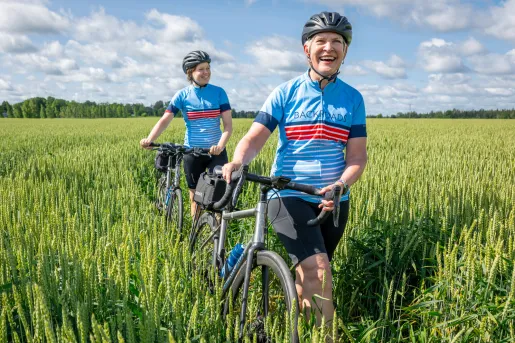Two women smiling while walking their bikes in tall weeds in a valley