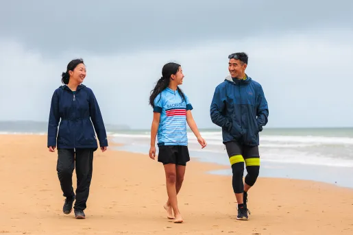 Two women and one man smiling while walking on a beach