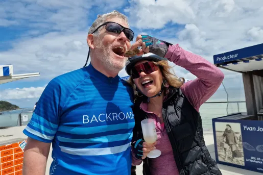 Man and woman smiling while holding up an oyster to eat