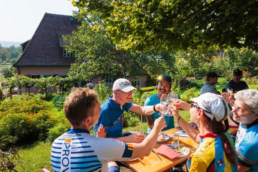 Group of people sitting at a table outdoors, raising their glasses of drinks