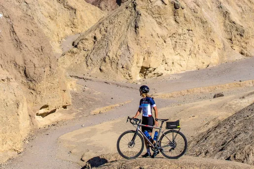 Woman standing next to her bike on a boulder, looking out to large canyons