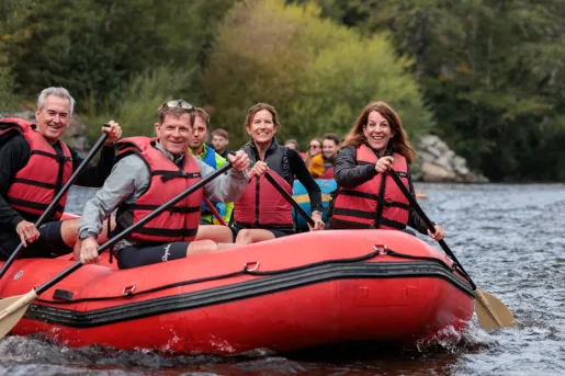 Group of people wearing life vests while paddling in a red raft on a river