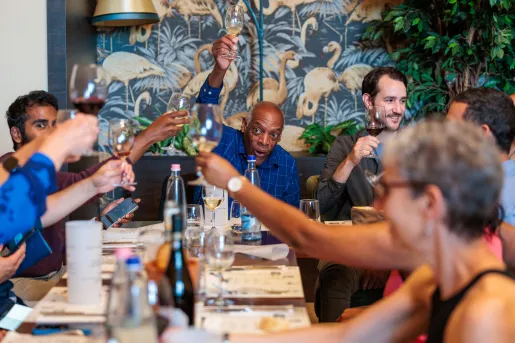 Group of people laughing and raising glasses of wine around a dining table