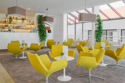 Indoor bar and lounge with yellow chairs and circular, white tables