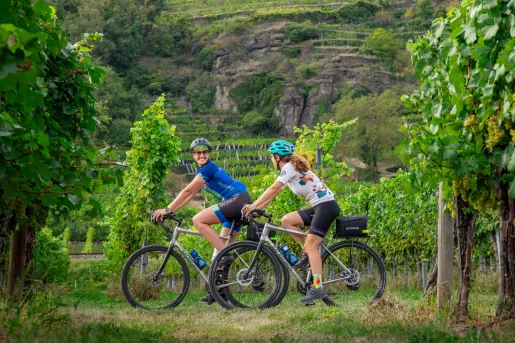 Two women looking at each other, smiling and biking through a vineyard