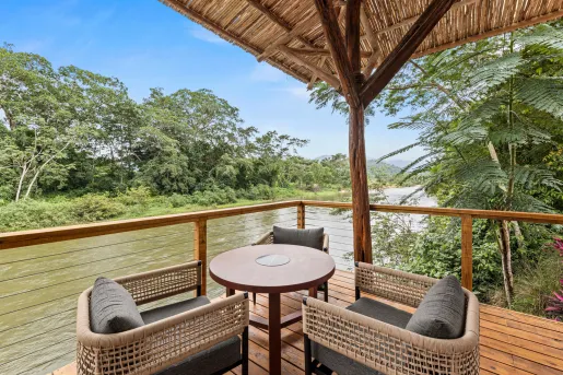 Outdoor balcony with two woven chairs and a circular table, with a river in the background