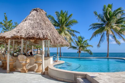 Outdoor pool with a straw hut to the left and the beach in the background