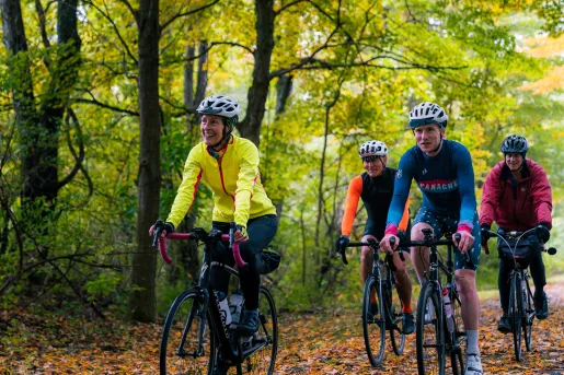 One woman and 3 men riding bikes on a road full of trees and leaves