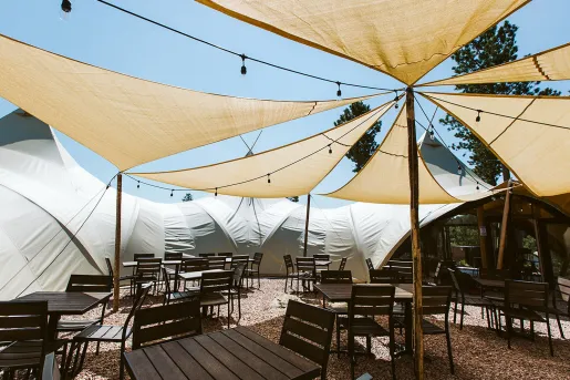 Outdoor patio on gravel, with large cloth sun shades and wooden chairs