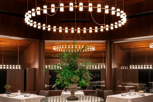 Restaurant with a circular light fixture and white dining tables around a floral centerpiece