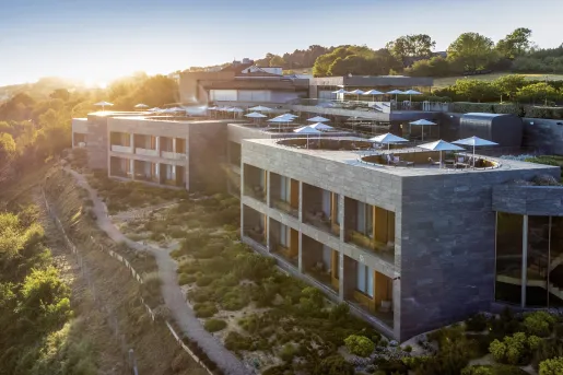 Exterior view of stone hotel building with a rooftop patio and trees in the distance