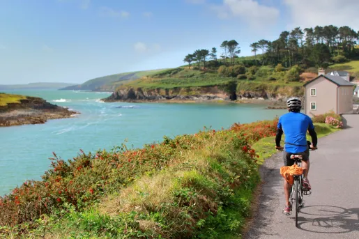 Man in a blue jersey, riding a bike on a road along a large lake