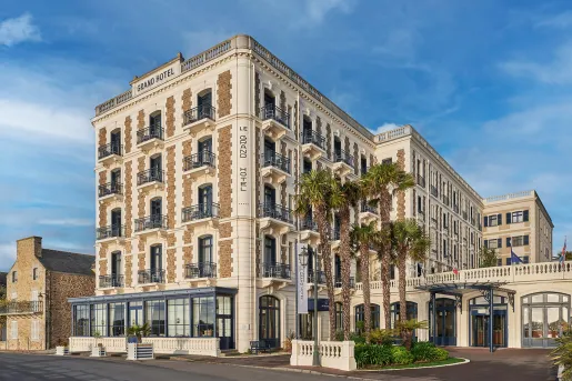 Exterior view of multi-story beige hotel building with palm trees in front