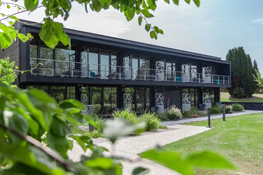 Exterior view of black, two-story building with outdoor balconies and a grass field in front