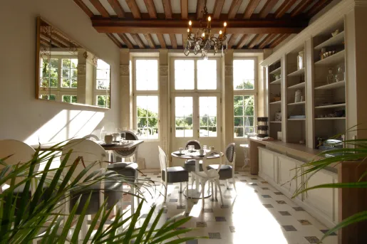 Kitchen with two dining tables and white and blue chairs, with large windows in the background