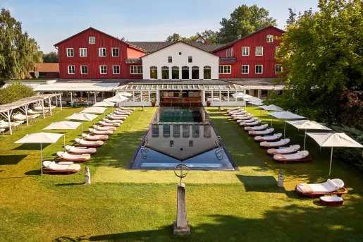 Red and white building with an outdoor pool in front, surrounded by reclining white chairs and white umbrellas