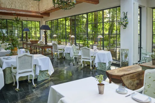 Dining area with square tables with white cloths, and large windows around the room