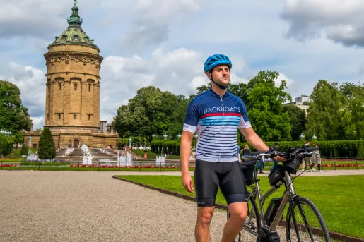 Man walking next to a bike, with a large castle-like building in the background
