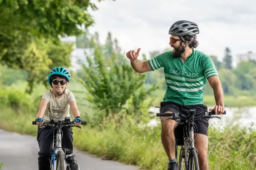Man and son riding their bikes on a road, with a lake on the right