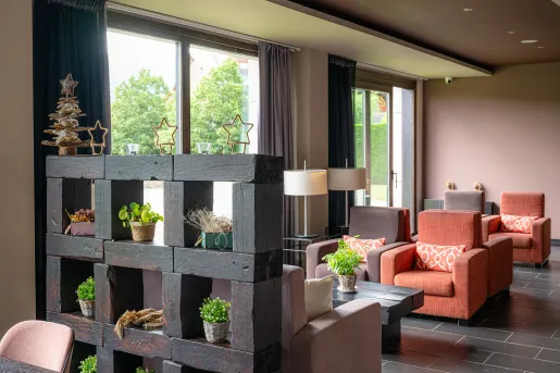 Indoor hotel reception area with cushioned chairs and plants scattered around the room