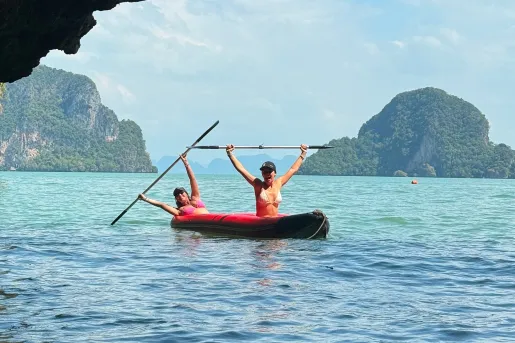 Two women on a red kayak, holding their paddles in the air