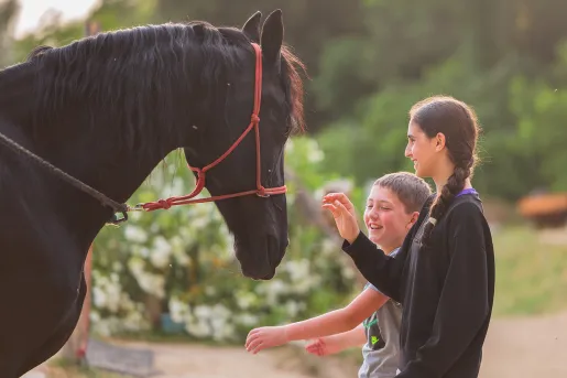 Little boy and older girl smiling while petting a black horse