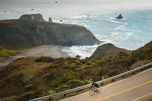 Person riding a bike on an empty road, with views of the ocean in  the distance