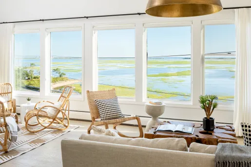 White room with wooden furniture and large windows looking out to a marsh
