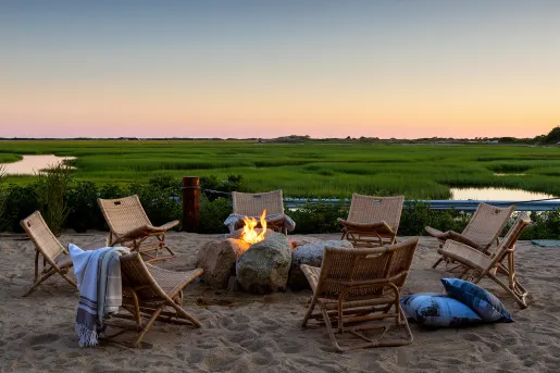 Sandy patio with woven chairs and a firepit, with a large marsh in the background
