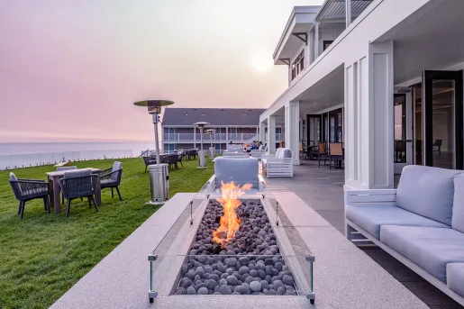 Outdoor patio in front of a white building with cushioned chairs and open fire pits