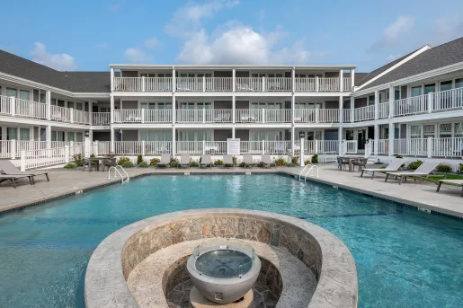 Outdoor pool with a fountain in the center and hotel building in the back
