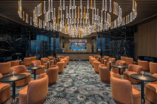 Bar and lounge with orange, cushioned chairs and a large chandelier hanging from the ceiling