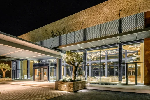 Exterior view of stone hotel building with large windows and trimmed trees in front