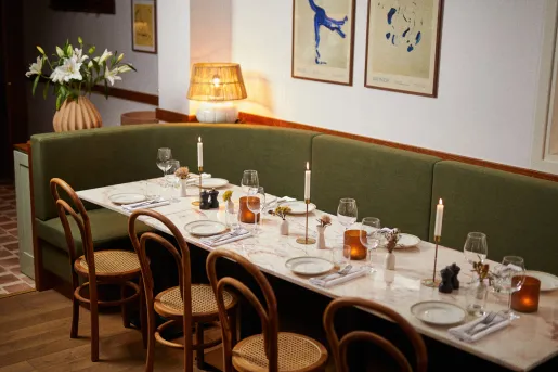 Long dining table with green couches and wooden chairs, with paintings on the walls