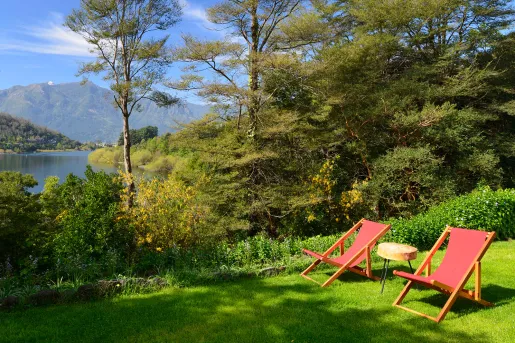 Two red chairs on a field of grass, looking out towards a lake surrounded by trees